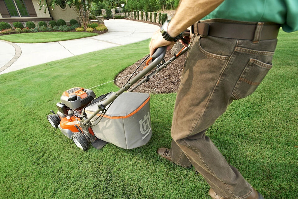 A person pushing a lawn mower across a freshly cut lawn