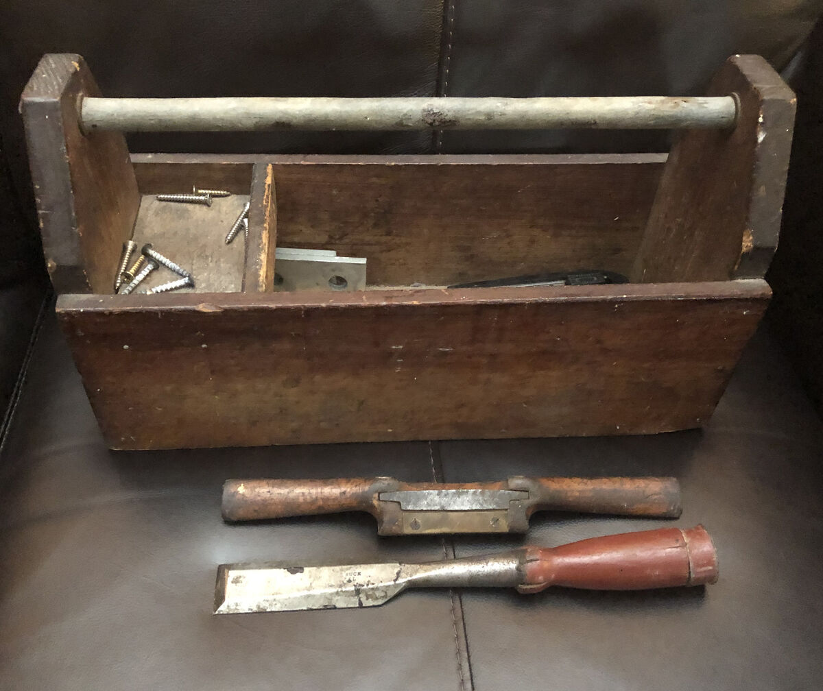 An old wooden toolbox with screws inside, a drawknife and a chisel in front of it